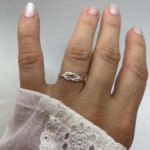Op de afbeelding: Een zilveren knoop ring aan een vinger. De ring is simpel en delicaat, met een gladde afwerking.