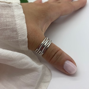 Op de afbeelding: Een set van vier zilveren duimringen gestapeld op een vinger. De ringen hebben verschillende texturen, waaronder een gladde band, een getextureerde band en een band met kleine kralen.