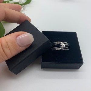 May include: A silver ring with three bands, each with a textured design. The ring is in a black velvet box.