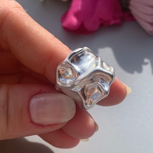May include: A silver ring with a unique, abstract, and textured design. The ring is made of a smooth, shiny metal and has a modern, contemporary style.