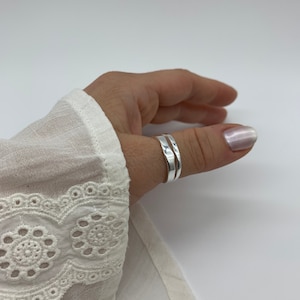 Puede incluir: Dos anillos de pulgar de plata apilados uno encima del otro en el pulgar de una persona.
