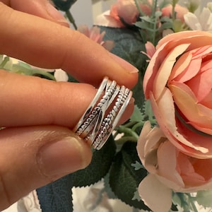 May include: A silver ring featuring a multi-band design with three distinct textures. The band includes a central twisted rope pattern flanked by two beaded bands and two smooth, plain silver bands, creating a layered appearance on the finger.