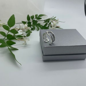 May include: A silver ring with a double band design. The ring is in a gray box.