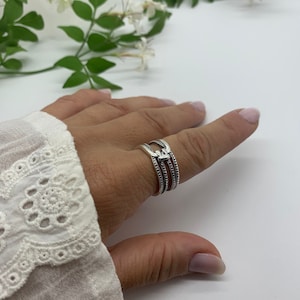May include: A silver ring with three bands and a heart design. The ring is on a person's finger.