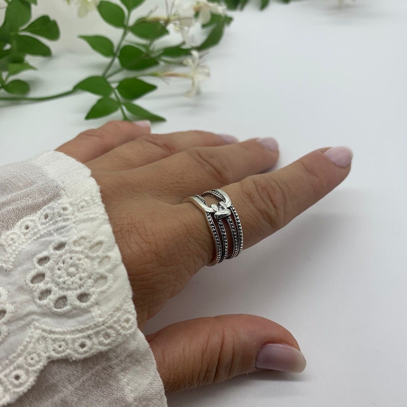May include: A silver ring with three bands and a heart design. The ring is on a person's finger.