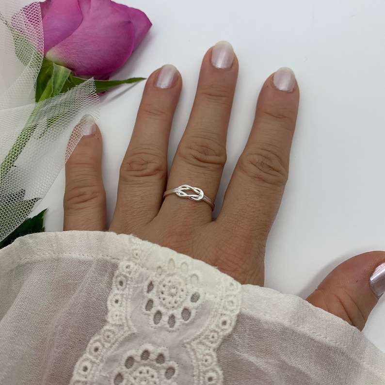 Op de afbeelding: Een zilveren ring met een knoopdesign. De ring zit aan een vinger.