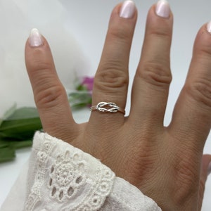 Op de afbeelding: Een zilveren knoop ring aan een vinger. De ring is simpel en delicaat, met een gladde afwerking.