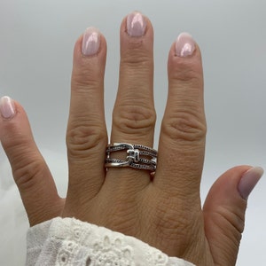 May include: A silver ring with a triple band design. The center band features a textured, geometric shape.