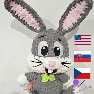 May include: A grey crocheted bunny rabbit with pink ears, white fur on the face, and a green bow tie. The bunny is holding a green yarn ball with a crochet hook. The image also includes the flags of the United States, Slovakia, and the Czech Republic.