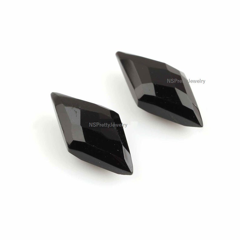May include: Two black diamond-shaped gemstones with a faceted cut. The gemstones are on a white background.
