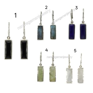 Puede incluir: Una colección de cinco pares de pendientes rectangulares de piedras preciosas. Los pendientes presentan una variedad de piedras, incluyendo ónix negro, labradorita, lapislázuli, verde y piedra lunar blanca, engastadas en metal plateado. Cada pendiente tiene un cierre de palanca.