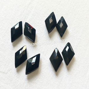 May include: Ten black diamond-shaped gemstones, each with a faceted surface. The gemstones are arranged in a scattered pattern on a white surface.