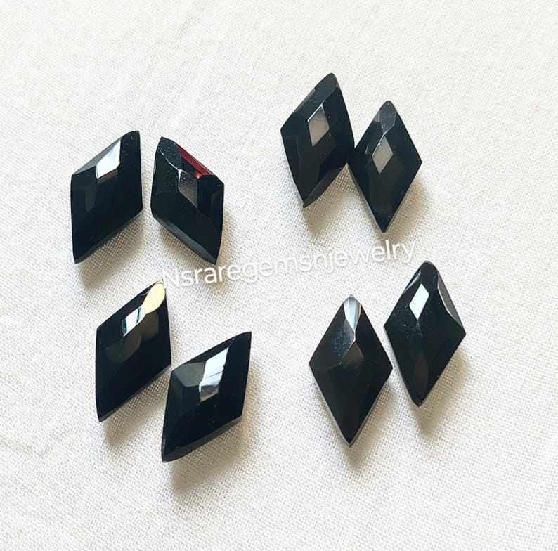 May include: Ten black diamond-shaped gemstones, each with a faceted surface. The gemstones are arranged in a scattered pattern on a white surface.