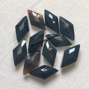 May include: A collection of twelve black and brown diamond-shaped gemstone cabochons. The cabochons are faceted and have a polished finish.