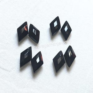 May include: Seven black diamond-shaped faceted glass gems with a silver reflective surface. The gems are arranged in a random pattern on a white surface.