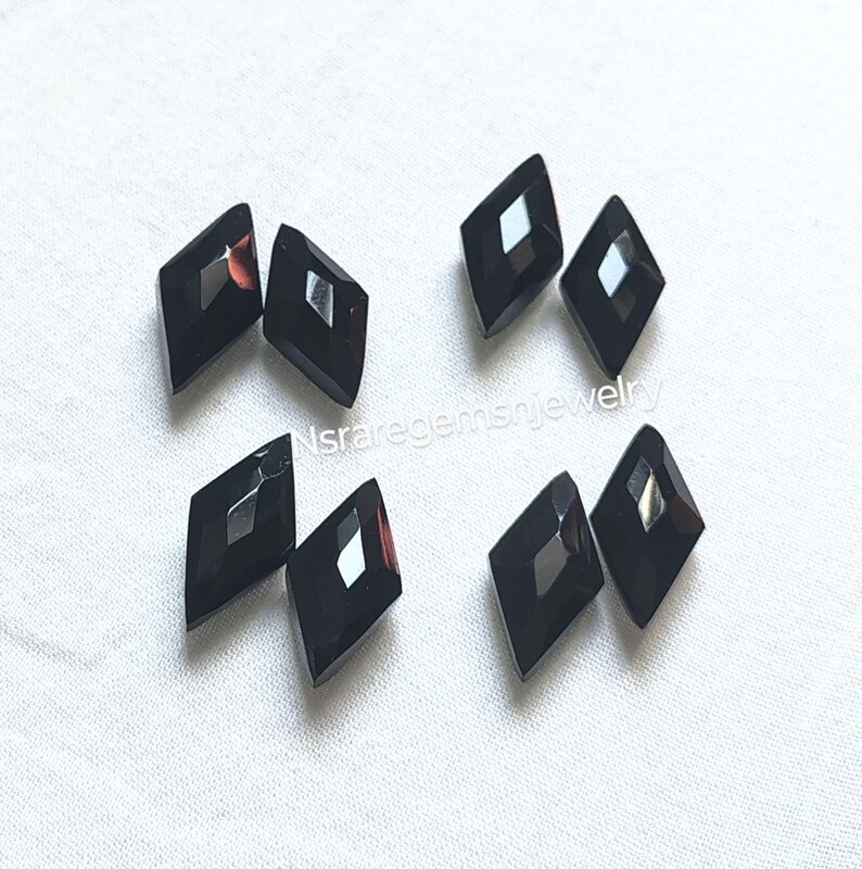 May include: Seven black diamond-shaped faceted glass gems with a silver reflective surface. The gems are arranged in a random pattern on a white surface.