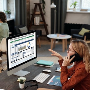 Pu&ograve; includere: Una donna al telefono indica uno schermo di computer che mostra un cruscotto finanziario e contabile con grafici e diagrammi. Il cruscotto include un grafico a torta, grafici a barre e una tabella di dati. Il testo sullo schermo recita "Cruscotto finanziario e contabile - Profitti e perdite".