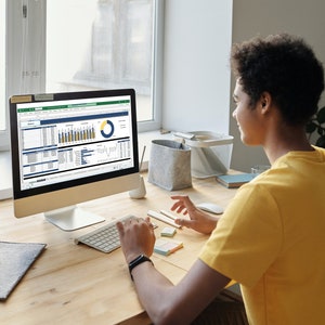 Pu&ograve; includere: Una persona seduta a una scrivania davanti a uno schermo di computer. Lo schermo mostra un foglio di calcolo con grafici e diagrammi. La persona sta usando una tastiera e un mouse per navigare nel foglio di calcolo.