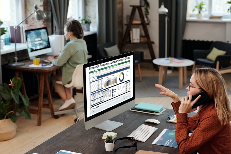 Pu&ograve; includere: Una donna al telefono indica uno schermo di computer che mostra un cruscotto finanziario e contabile con grafici e diagrammi. Il cruscotto include un grafico a torta, grafici a barre e una tabella di dati. Il testo sullo schermo recita "Cruscotto finanziario e contabile - Profitti e perdite".