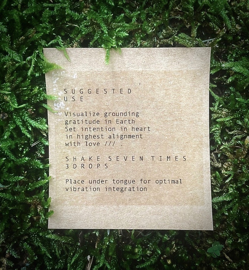 Op de afbeelding: Een bruine papieren kaart met instructies voor het gebruik van een product. De tekst luidt: "SUGGESTED USE Visualize grounding gratitude in Earth Set intention in heart in highest alignment with love ///. SHAKE SEVEN TIMES 3DROPS Place under tongue for optimal vibration integration"