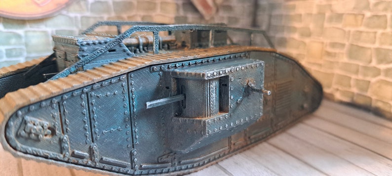 Op de afbeelding: Een gedetailleerd model van een tank uit de Eerste Wereldoorlog, geverfd in een donker teal kleur. De tank heeft een verhoogd, open dak en een groot, rechthoekig luik aan de achterkant. Het model is gemaakt van plastic en heeft een realistische, verweerde uitstraling.