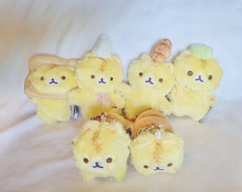 May include: A set of six yellow plush toys shaped like bears. The bears are wearing different hats and accessories, including a unicorn horn, a bun, and a green leaf.
