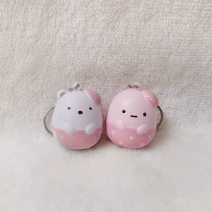 May include: Two small, white and pink, squishy keychain toys shaped like cartoon characters with strawberry accents. The characters have black eyes and mouths.