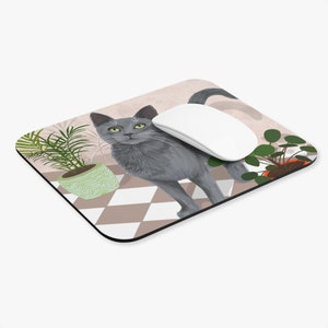 May include: A grey cat with green eyes stands on a chequered floor with two potted plants. A white computer mouse is on the floor next to the cat. The mouse pad is a light brown colour with a pink background.