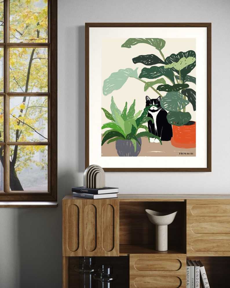 May include: A black and white cat sits in a pot of green plants. The cat is looking to the left of the image. The plants are in a room with a window and a wooden shelf. The text "FROM HERE" is at the bottom of the image.
