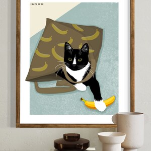 K&ouml;nnte beinhalten: Eine schwarz-wei&szlig;e Katze mit gr&uuml;nen Augen schaut aus einer braunen Tragetasche mit Bananenmuster. Die Katze h&auml;lt eine gelbe Banane in ihrer Pfote. Das Bild tr&auml;gt den Text "FROM BURU" oben links.