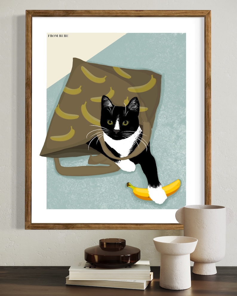 K&ouml;nnte beinhalten: Eine schwarz-wei&szlig;e Katze mit gr&uuml;nen Augen schaut aus einer braunen Tragetasche mit Bananenmuster. Die Katze h&auml;lt eine gelbe Banane in ihrer Pfote. Das Bild tr&auml;gt den Text "FROM BURU" oben links.