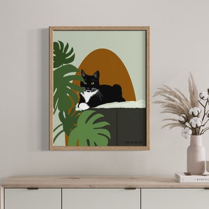 May include: A framed illustration of a black and white cat with green eyes, lounging on a ledge with a green monstera plant in the background. The illustration has a muted green, brown, and orange color palette. The text "FROM HERE" is at the bottom of the illustration.