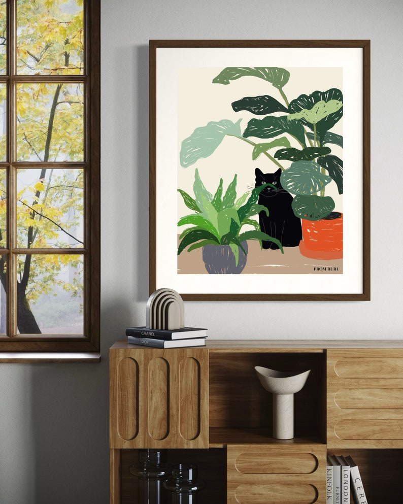 May include: A framed illustration of a black cat sitting in a pot of plants. The plants are green and the pot is orange. The background is a light beige color. The text "FROM RURU" is at the bottom of the illustration.
