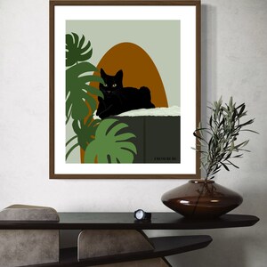 May include: A framed print of a black cat sitting on a ledge with green tropical plants and a brown and orange background. The print has the text "FROM RURY" at the bottom.