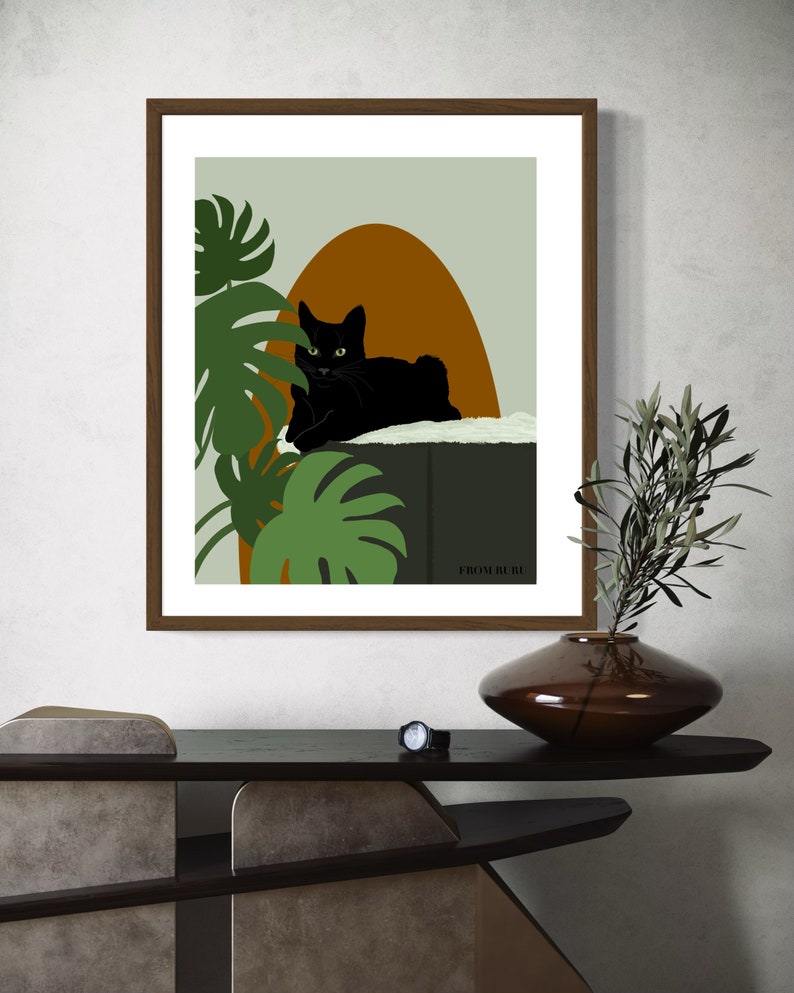 May include: A framed print of a black cat sitting on a ledge with green tropical plants and a brown and orange background. The print has the text "FROM RURY" at the bottom.