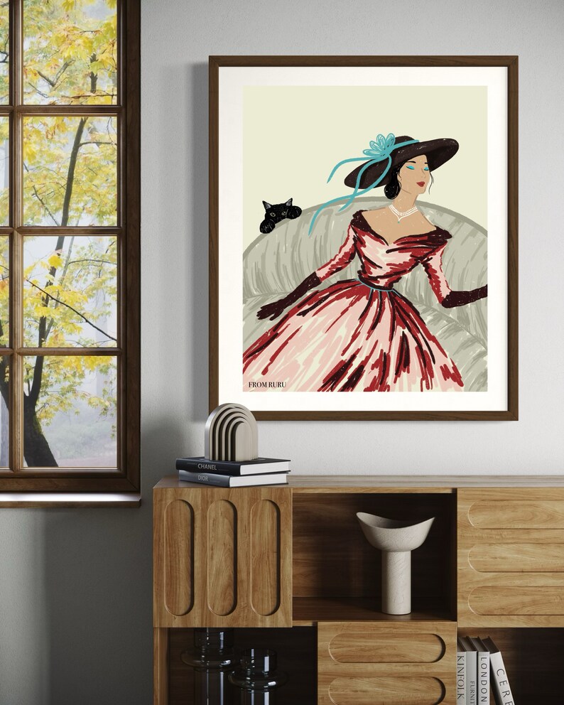 May include: A framed illustration of a woman wearing a red and pink dress and a large hat with a blue ribbon. She is sitting on a couch with a black cat beside her. The text "From Ruru" is at the bottom of the illustration.