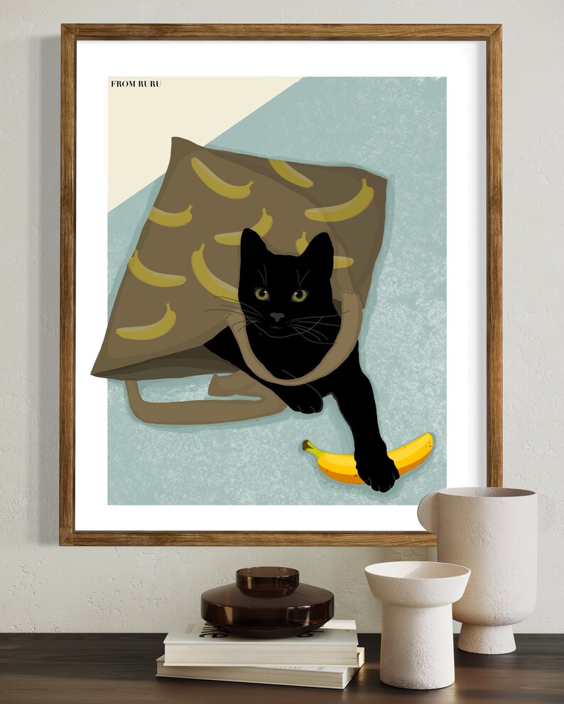 K&ouml;nnte beinhalten: Eine schwarze Katze mit gr&uuml;nen Augen schaut aus einer braunen Tragetasche mit Bananenmuster. Die Katze h&auml;lt eine gelbe Banane in ihrer Pfote. Der Text "FROM RURU" befindet sich in der oberen linken Ecke des Bildes.
