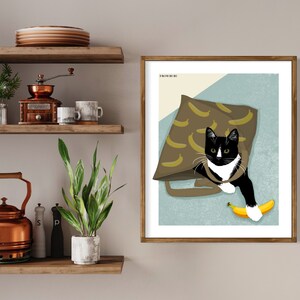 K&ouml;nnte beinhalten: Eine schwarz-wei&szlig;e Katze mit gr&uuml;nen Augen sitzt in einer braunen Tasche mit Bananenmuster. Die Katze h&auml;lt eine gelbe Banane in ihrer Pfote. Das Bild ist mit "From Rue" betitelt.