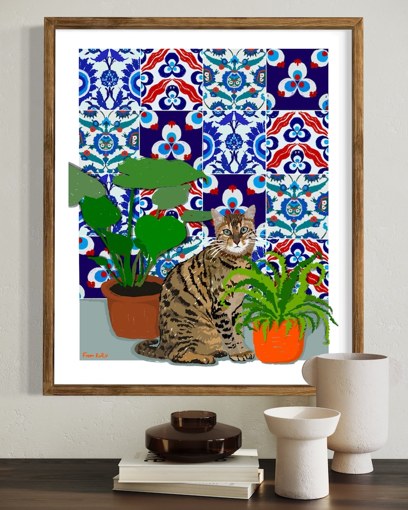 May include: A framed print of a tabby cat sitting in front of a tiled wall with two potted plants. The tiles are blue, red and white with intricate patterns. The print is signed "Fram Ru."