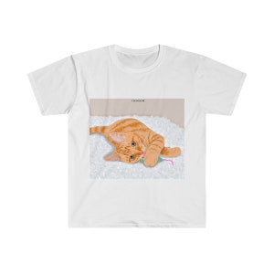 May include: A white t-shirt with a graphic of an orange tabby cat playing with a pink and green toy mouse on a white fluffy surface.