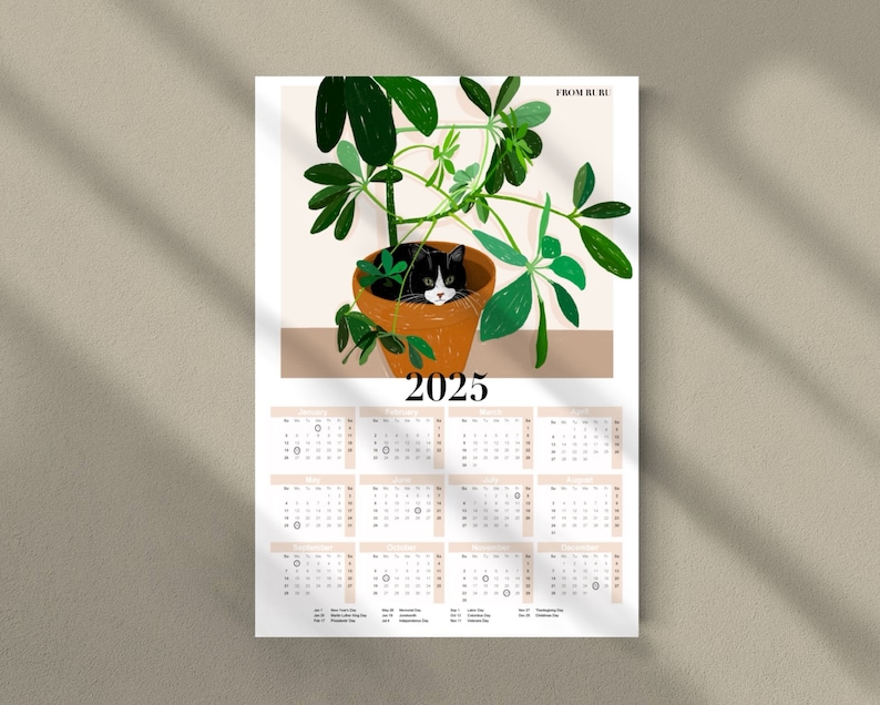 Pu&ograve; includere: Un calendario 2025 con un gatto bianco e nero rannicchiato in una pianta in vaso. La pianta ha grandi foglie verdi e il vaso &egrave; marrone. Il calendario &egrave; stampato su carta bianca con testo nero.
