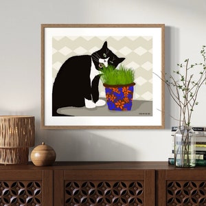 Peut inclure: Un chat noir et blanc avec une tache blanche sur la poitrine mange de l'herbe dans un pot bleu et orange &agrave; motif floral. Le chat est assis sur une surface brun clair. L'arri&egrave;re-plan est beige clair avec un motif en chevron.