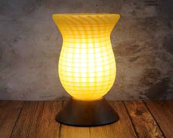 May include: A yellow glass oil diffuser with a checkered pattern and a brown base. The diffuser is lit and glowing.