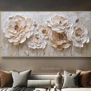 May include: A rectangular floral painting in a gold frame. The artwork features textured, three-dimensional white and peach-coloured peony flowers. The painting is displayed above a sofa with decorative cushions.