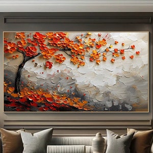 May include: A large framed abstract painting featuring a tree with vibrant orange and red blossoms. The tree's dark trunk and branches contrast against a textured, gray and white background. The artwork is displayed above a sofa in a living room setting.
