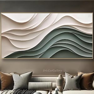 May include: Abstract wall art featuring a layered design with flowing, wave-like forms in shades of white, beige, and green. The artwork is framed in gold and hangs above a sofa with decorative pillows.