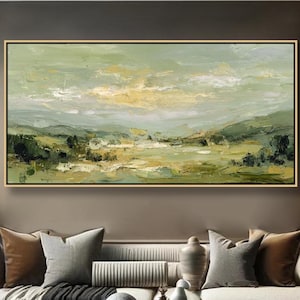 May include: An abstract landscape painting in a gold frame, featuring a palette of greens, yellows, and blues. The artwork depicts rolling hills and a cloudy sky. The painting hangs above a white sofa with decorative pillows, a dark coffee table, and decorative vases.