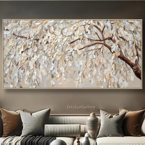 May include: A large rectangular oil painting of a tree with textured, off-white leaves and brown branches. The artwork is framed in gold and hangs above a white sofa with decorative cushions. The room has a modern, neutral colour scheme.