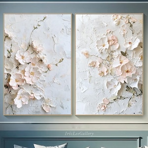 May include: Two framed abstract paintings with a textured white background and pink and white flowers. The paintings are hanging on a blue wall.