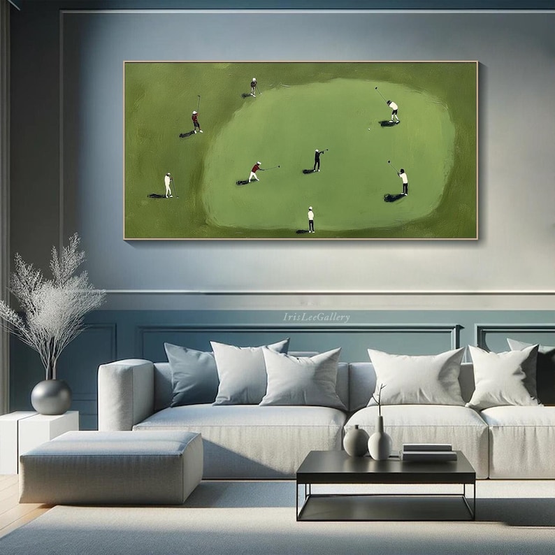May include: An abstract painting of a golf course with golfers in action. The artwork features a green field with several figures in white and red attire, swinging golf clubs. The painting is framed in gold and hangs above a gray sofa.